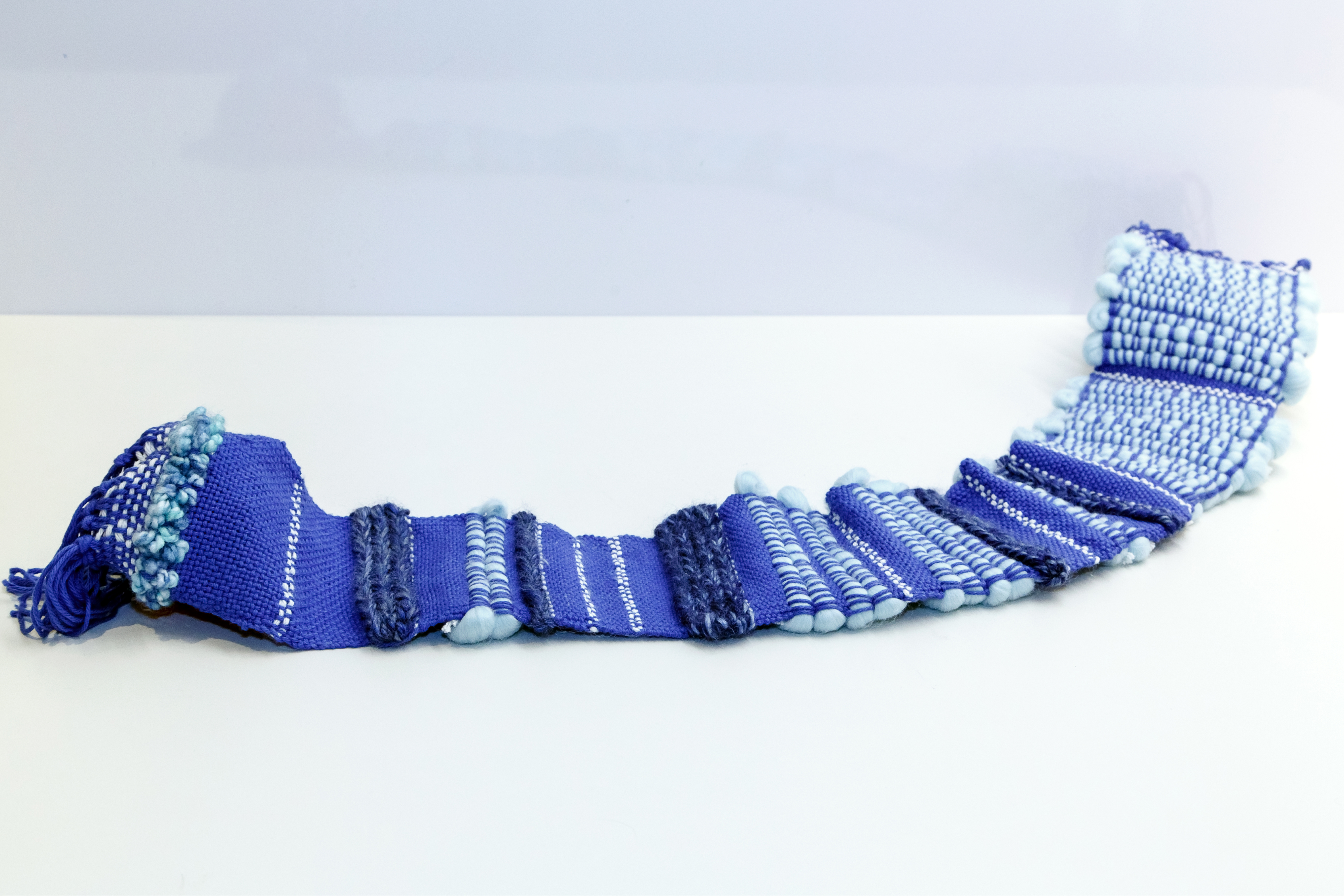 A scarf with alternating bands of blue fabrics resting on a table.