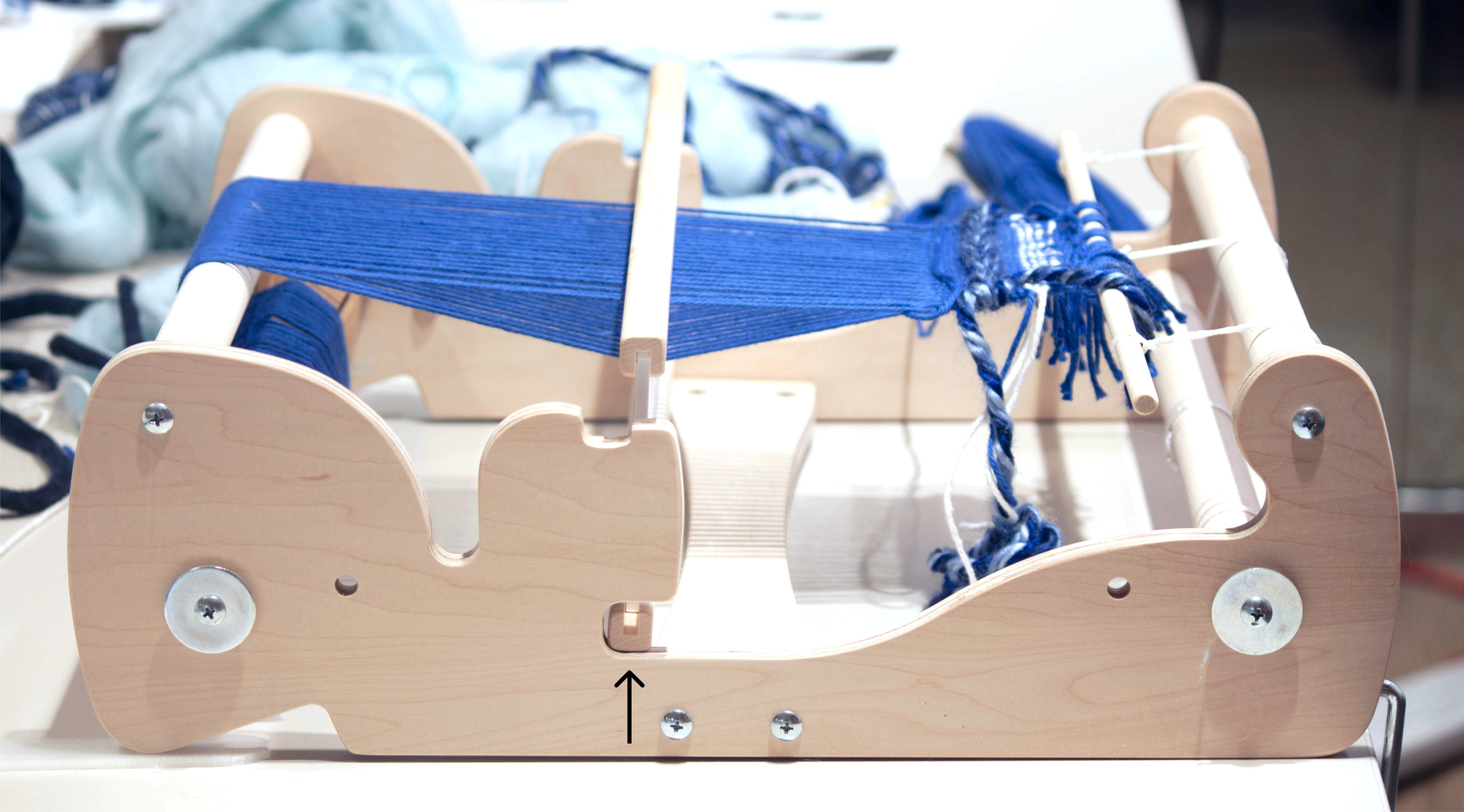 Wooden loom sitting on table with blue thread strung taught, pulled downwards.