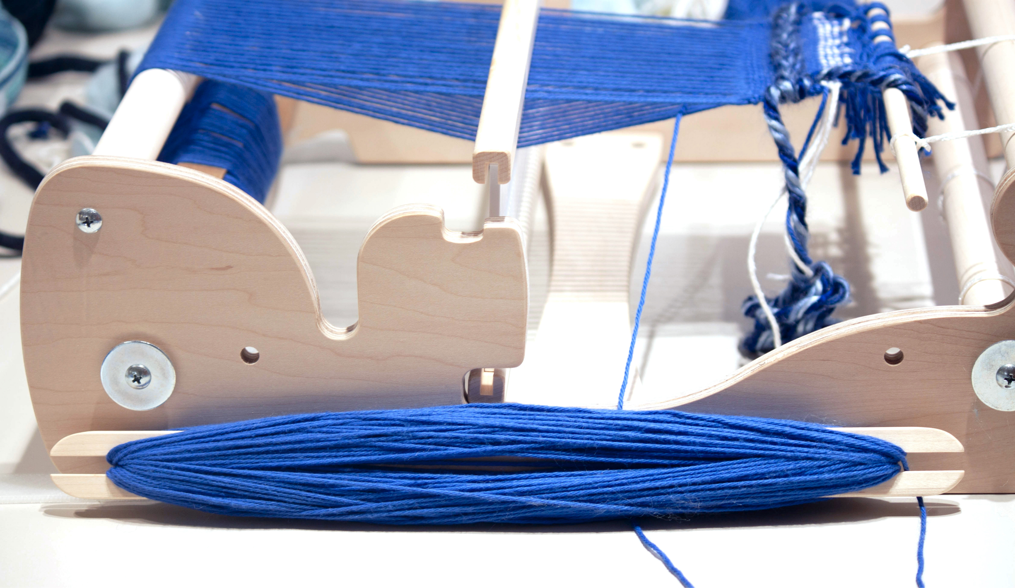 Close-up of wooden loom showing long wooden rod with blue yarn wrapped around it.
