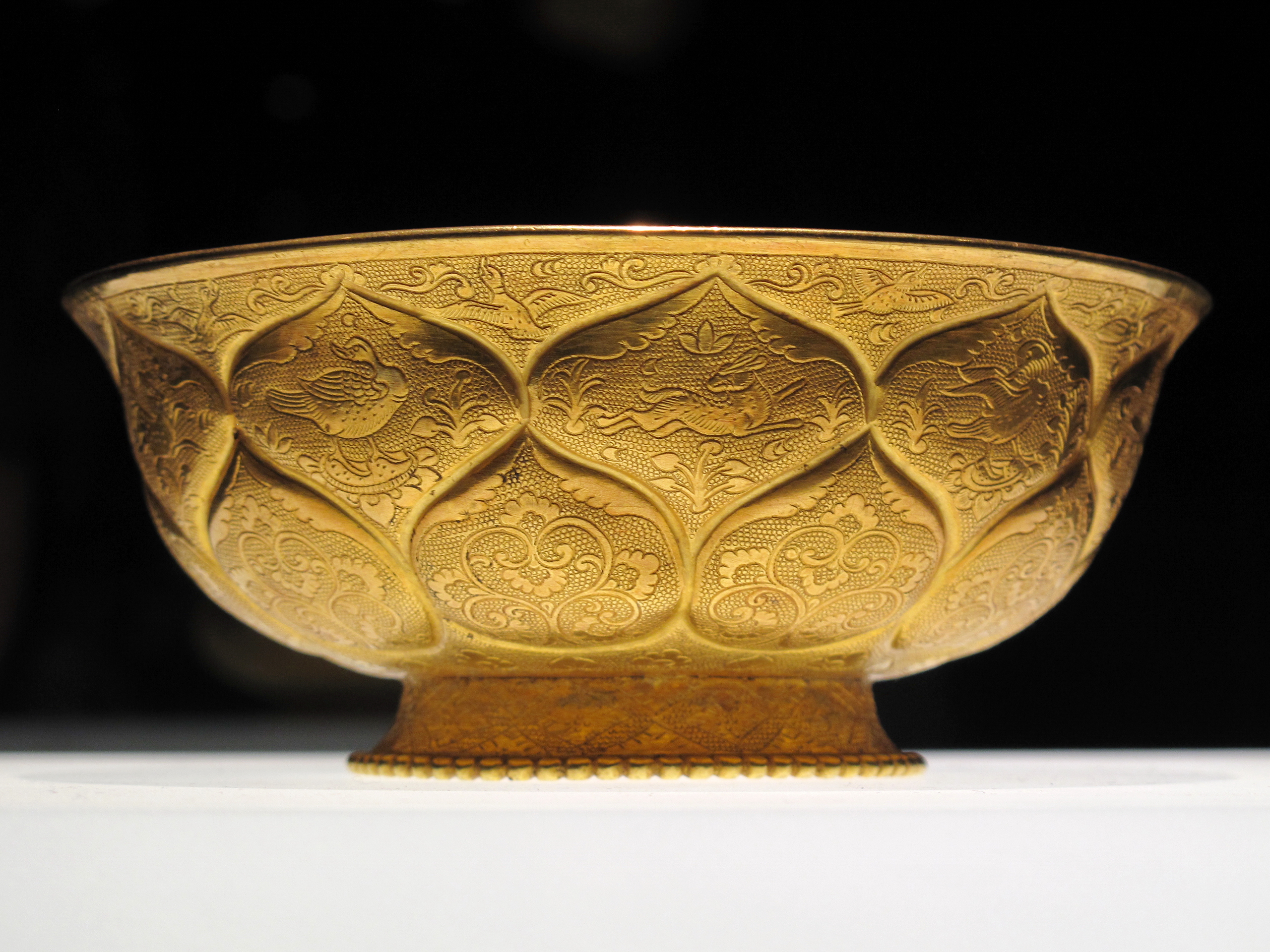 A golden bowl with decorative patterns and animals engraved along the side.
